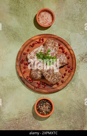 Blick von oben auf georgianische Roh-Rind- oder Lammkoteletts - Apkhazura mit Gewürzen und Kräutern auf hölzernem Schneidebrett Stockfoto