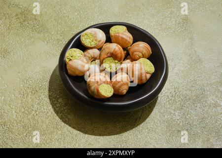 Essbare Schnecken gefüllt mit würziger Kräuterbutter in schwarzer Schüssel Stockfoto