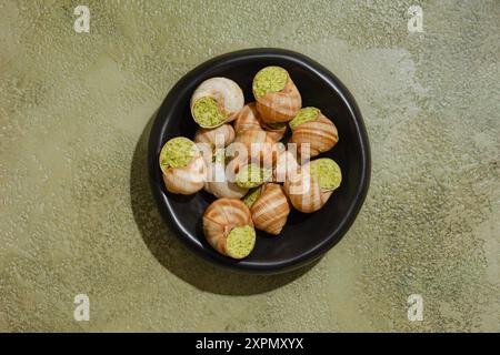 Blick von oben auf essbare Schnecken, gefüllt mit würziger Kräuterbutter in schwarzer Schüssel Stockfoto