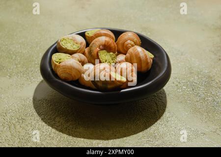 Essbare Schnecken Escargot gefüllt mit würziger Kräuterbutter auf grünem Hintergrund Stockfoto