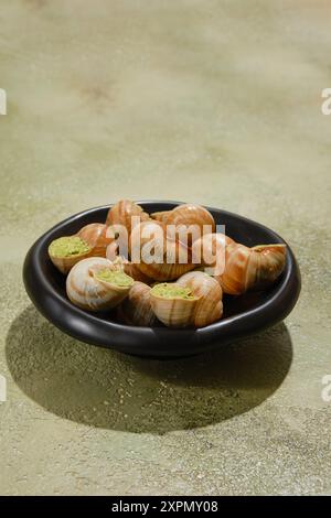 Schwarzer Teller voller Escargot-Schnecken, gefüllt mit scharfer Butter und Koriander Stockfoto