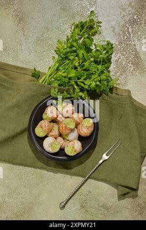 Über-Kopf-Komposition von in Soße gebackenen und mit Kräuterwürzbutter gefüllten Speiseschnecken auf einem Teller Stockfoto