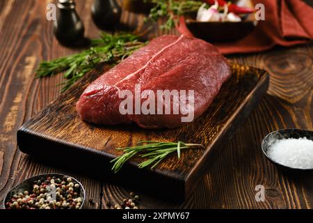 Rohes Rindersteak mit oberer Klinge auf hölzernem Schneidebrett, umgeben von Gewürzen und Kräutern Stockfoto