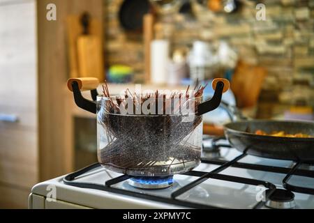 Kochen von schwarzen Reisnudeln in einem transparenten Glastopf auf einem Gasherd in der Küche Stockfoto