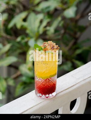 Ein erfrischender Cocktail in einem hohen Glas. Leuchtende Schichten aus Rot, Orange und Gelb werden mit einem Minzzweig und einem zarten Crumble gekrönt Stockfoto