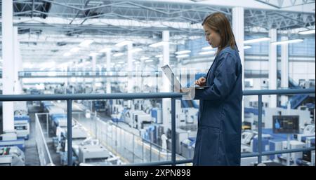 Porträt eines schönen japanischen Ingenieurs, der einen Laptop benutzt und sich in einer Fabrik umsieht, in der Geräte zur Herstellung moderner elektronischer Bauteile für verschiedene Branchen hergestellt werden Stockfoto