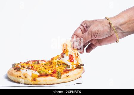 Die Hand der indischen Frau trägt einen goldenen Armreif und nimmt köstliche vegetarische Paneer-Pizza auf weißem Hintergrund. Nahaufnahme Stockfoto