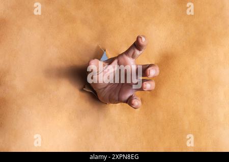 Die Hand kommt aus einem Loch in einem braunen Papier. Nahaufnahme Stockfoto