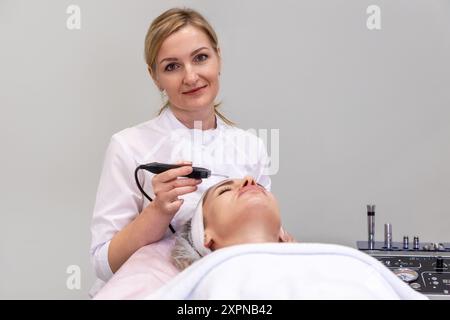 Professionelle Kosmetikerin führt Ultraschallpeeling-Reinigung im Gesicht einer jungen kaukasischen Frau durch. Hardware-Apparatekosmetologie. Kopierbereich. Stockfoto