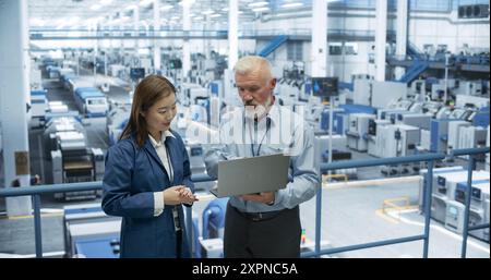 Erfahrener Ingenieur mittleren Alters, der jungen japanischen Schülern eine Tour durch die Elektronikfabrik unterhält. Asiatische Frau mit technischem Hintergrund stellt Fragen zu Produktion, Fertigung, Forschung Stockfoto