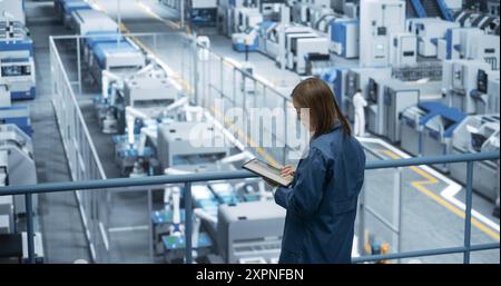 Porträt eines schönen japanischen Ingenieurs, der einen Tablet-Computer benutzt und sich in einer Fabrik umsieht, in der Geräte zur Herstellung moderner elektronischer Komponenten für verschiedene Branchen hergestellt werden Stockfoto