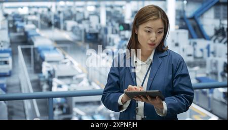 Porträt eines schönen japanischen Ingenieurs, der einen Tablet-Computer benutzt und sich in einer Fabrik umsieht, in der Geräte zur Herstellung moderner elektronischer Komponenten für verschiedene Branchen hergestellt werden Stockfoto