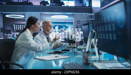 Biotechnologie-Medizinisches Forschungszentrum: Asiatische Neurowissenschaftlerin Mit Desktop-Computer Und Gespräch Mit Männlichem Kaukasischen Chirurgen Mit Mikroskop. Spezialisten Entwickeln Innovative Krebsbehandlung. Stockfoto