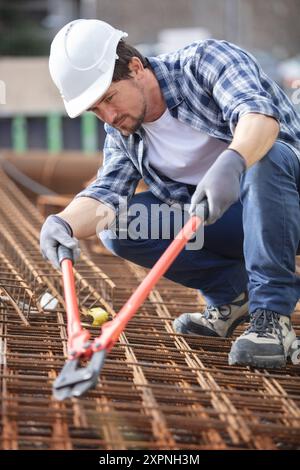 Arbeiter, der Bolzenschneider an Metall-Bewehrungsstäben verwendet Stockfoto