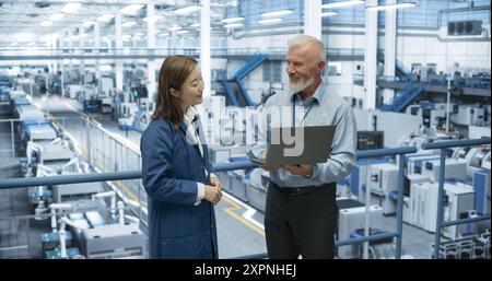 Erfahrener Ingenieur mittleren Alters, der jungen japanischen Schülern eine Tour durch die Elektronikfabrik unterhält. Asiatische Frau mit technischem Hintergrund stellt Fragen zu Produktion, Fertigung, Forschung Stockfoto