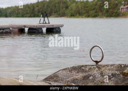 Festmacherring für Boote im Stein, alter grauer Holzsteg, Ponton auf dem Hintergrund im Golf von Finnland, Ostsee Stockfoto