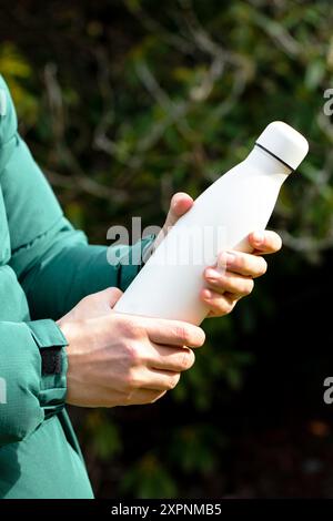 Der Mann hält eine Modell-Thermoskanne gegen verschwommene Büsche aus der Nähe Stockfoto