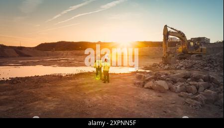 Luftdrohnenaufnahme der Baustelle mit Baggern am sonnigen Tag: Ein Team von Immobilienentwicklern diskutiert das Projekt. Bauingenieur, Architekt, Inspektor Spricht, Mit Tablet-Computer. Stockfoto
