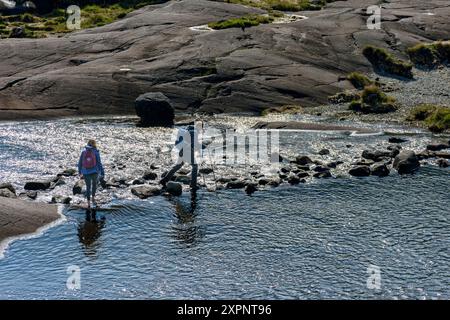 Zwei Wanderer überqueren die Trittsteine über den Scavaig River in der Nähe des Ausgangs Loch Coruisk, Isle of Skye, Schottland, Großbritannien. Stockfoto