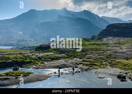 Wanderer überqueren die Trittsteine über den Scavaig River in der Nähe des Ausgangs Loch Coruisk, Isle of Skye, Schottland, Großbritannien. Die Cuillin Berge dahinter Stockfoto