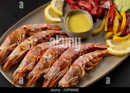 Gegrillte Garnelen auf Teller mit Zitronenscheibe und Gemüse. Meeresfrüchte im Hintergrund. Stockfoto