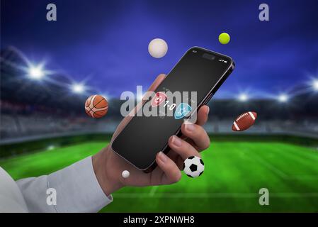 Telefon in Hand mit einer Live-Score-App, die auf dem Bildschirm vor dem Hintergrund eines Fußballstadions angezeigt wird. Sportbälle fliegen am Telefon herum, Emphas Stockfoto