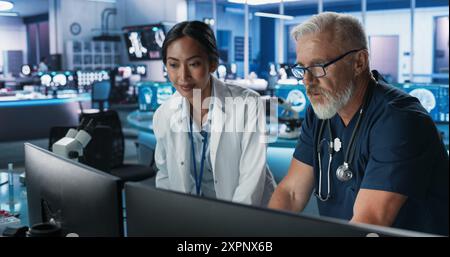 Asiatische Wissenschaftlerin Mit Desktop-Computer Und Gespräch Mit Kaukasischen Männlichen Doktor Im Medizinischen Krankenhaus Research Lab. Kollegen Diskutieren Testergebnisse Von Patienten, Behandlungsmethoden Und Medikamente. Stockfoto