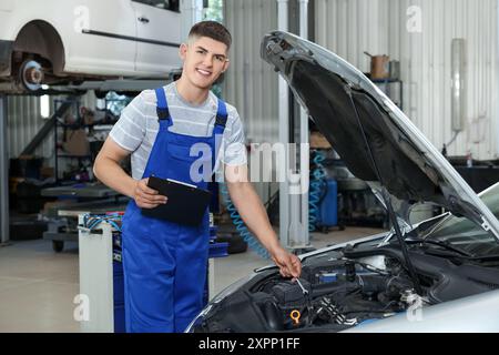 Junger Automechaniker macht Notizen während der Autodiagnose in der Autowerkstatt Stockfoto