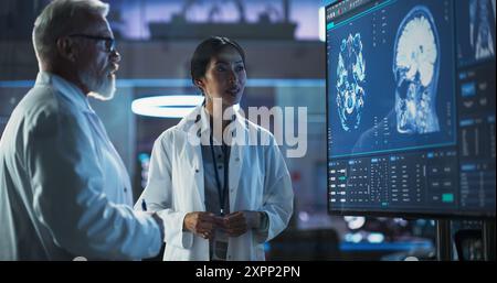 Neuroscience Laboratory Meeting: Asiatische Wissenschaftlerin und männliche kaukasische Chirurgin diskutieren MRT-Hirnscan auf TV-Display. Fachärzte Für Rehabilitationsmedikamente Nach Hirnschäden. Stockfoto