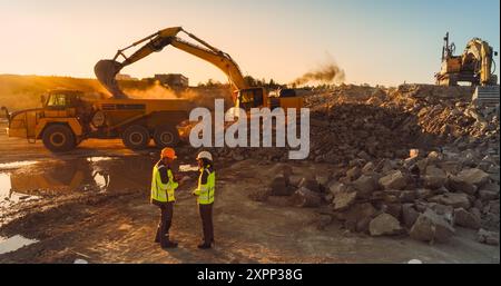 Luftdrohnenaufnahme der Baustelle am sonnigen Abend: Kaukasischer Bauingenieur spricht mit hispanischer Stadtplanerin und verwendet Tablet. Industriesbagger, der Steine in Einen Lkw lädt. Stockfoto