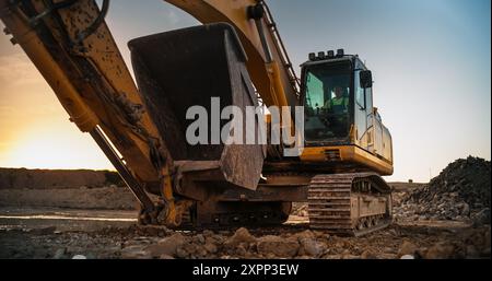 Baustelle Am Sonnigen Abend: Fahrt Mit Einem Industriesbagger Zur Fertigstellung Der Arbeiten Im Zusammenhang Mit Dem Bau Eines Neuen Immobilienprojekts. Mann, Der Schwere Maschinen Betreibt, Um Einen Wohnkomplex Zu Bauen. Stockfoto