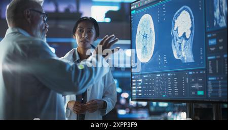 Neuroscience Laboratory Meeting: Asiatische Wissenschaftlerin und Chirurgin diskutieren MRT-Hirnscan auf TV-Display. Fachärzte Für Rehabilitationsmedikamente Nach Hirnschäden Stockfoto