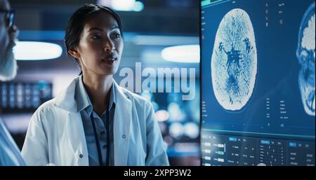 Neuroscience Laboratory Meeting: Close-up asiatische Wissenschaftlerin und männlicher Chirurg diskutieren MRT Brain Scan auf TV Display. Fachärzte Für Rehabilitationsmedizin Nach Schlaganfall Stockfoto