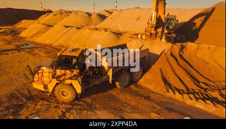 Luftdrohnenaufnahme der Baustelle am sonnigen Abend: Industriesbagger laden Sand in Einen Lkw. Der Prozess Des Neubaus Eines Wohnkomplexes. Konzept Für Arbeiter, Die Schwermaschinen Betreiben. Stockfoto