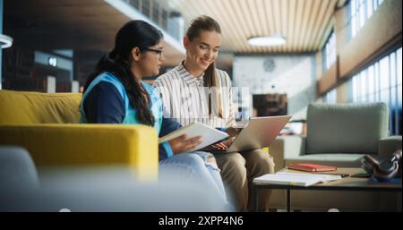 Zwei verschiedene Freunde und Klassenkameraden arbeiten an einem Teamprojekt in einer akademischen Bibliothek. Junge Inder- und Kaukasierinnen verwenden Laptop-Computer für Online-Lernen und virtuelle Vorlesungen Stockfoto
