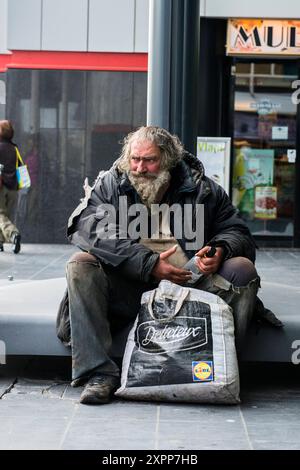 Vernachlässigter Alkoholiker Ein vernachlässigter alkoholischer Mann, der an einem Lampenmast in der Stadt den haag, Niederlande, sitzt und eine leere Weinflasche hält. Den Haag, s-Gravenhage Passage Centraal Station Zuid-Holland Nederland Copyright: XGuidoxKoppesxPhotox Stockfoto