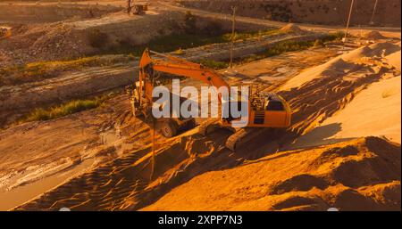 Luftdrohnenaufnahme der Baustelle am sonnigen Abend: Industriesbagger laden Sand in Einen Lkw. Der Prozess Des Bauens Eines Wohnblocks. Konzept Für Arbeiter, Die Schwermaschinen Betreiben. Stockfoto