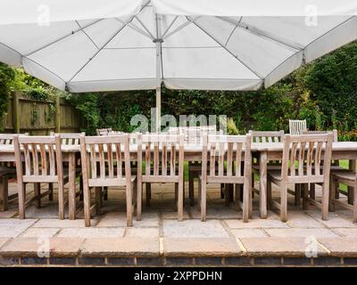 Terrasse mit Tisch und Stühlen unter einem Sonnenschirm in einem englischen Garten. Stockfoto