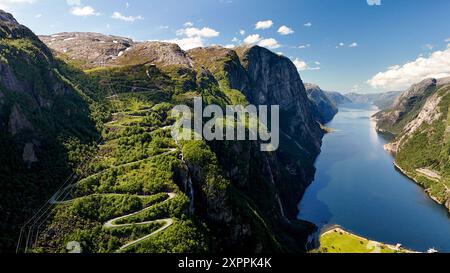 Erleben Sie den atemberaubenden Kontrast zwischen üppig grünen Berghängen und einem ruhigen Fjord unter einem klaren blauen Himmel, der Norwegens natürliche Schönheit und gewundene Straßen hervorhebt. Lysefjord Lysebotn Norwegen Stockfoto