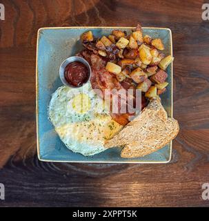 Traditionelles Frühstück mit Eiern, Speck, Toast und Bratkartoffeln auf einem grünen Teller Stockfoto