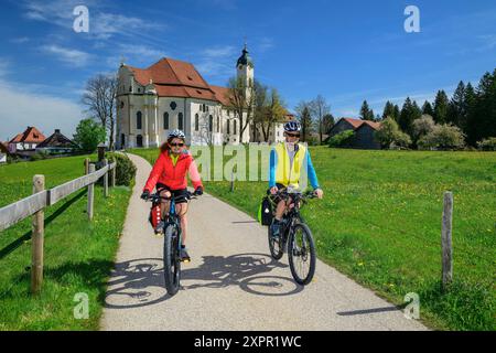 Mann und Frau Radfahren auf dem Bodensee-Königssee-Radweg mit Wieskirche im Hintergrund, wies, UNESCO-Weltkulturerbe Wieskirche, Oberbava Stockfoto