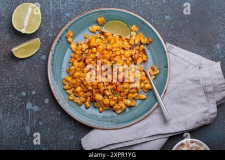 Teller mit Esquites mexikanischem Streetmaissalat mit Chili, Mayonnaise und Limette auf dunklem Steinhintergrund Stockfoto