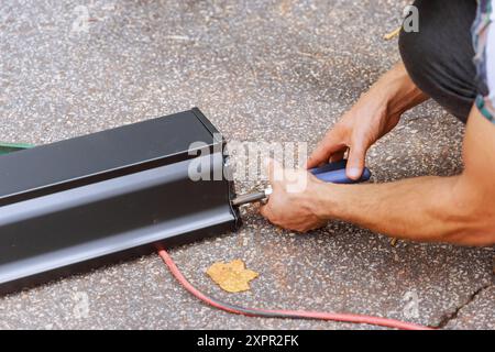 Arbeiter schneidet Aluminium-Regenrinnen mit Scheren, nachdem sie an der Maschine gebogen wurden Stockfoto