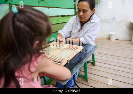 Mutter und Tochter genießen eine gute gemeinsame Zeit beim Spielen eines Backgammon-Spiels an einem sonnigen Tag zu Hause, was die Bindung der Familie fördert. Stockfoto