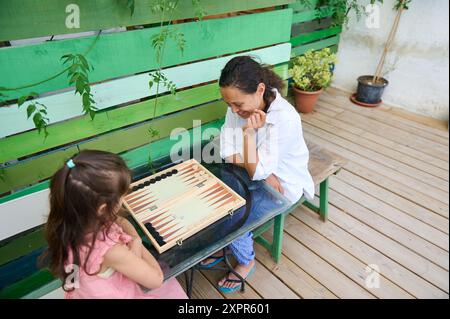 Mutter und Tochter verbrachten Zeit miteinander, um Backgammon zu spielen, und genießen einen sonnigen Tag auf einer begrünten Terrasse. Perfekte Momentkappe für Familienverbände Stockfoto