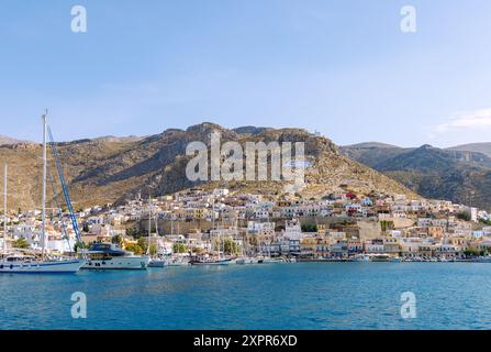 Inselhauptstadt Póthia, weiße Kapelle, griechische Flagge, pastellfarbene Häuser und Boote im Hafen auf der Insel Kalymnos (Kalimnos) in Griechenland Stockfoto