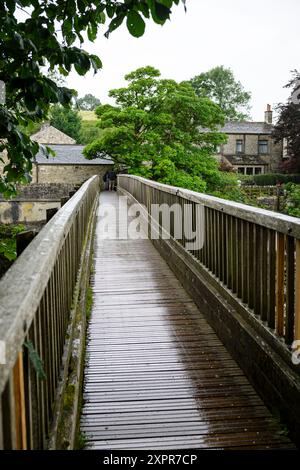 Grassington Yorkshire UK-27. Juli 2024. Eine ruhige hölzerne Brücke führt zu einem charmanten Dorf auf dem Land, umgeben von üppigem Grün. Stockfoto