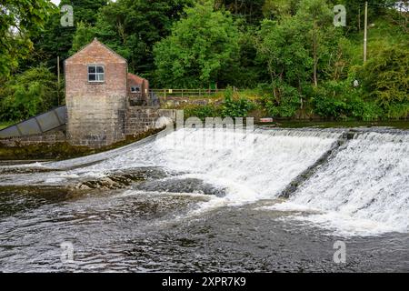 Grassington Yorkshire UK-27. Juli 2024. Altes Backsteingebäude an einem kaskadierenden Fluss in einer üppigen, grünen Waldlandschaft. Stockfoto