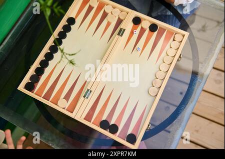 Hochwinkelansicht eines traditionellen Backgammon-Spiels auf einem Glastisch mit Brett, Schachteln und Würfeln. Das Bild erfasst einen Moment von relaxa Stockfoto