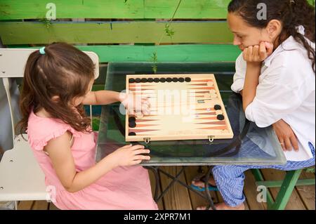 Mutter und Tochter spielen ein Spiel mit Backgammon und genießen gemeinsam schöne Zeit im Freien. Familienverbundenheit und Freizeitaktivitäten. Stockfoto